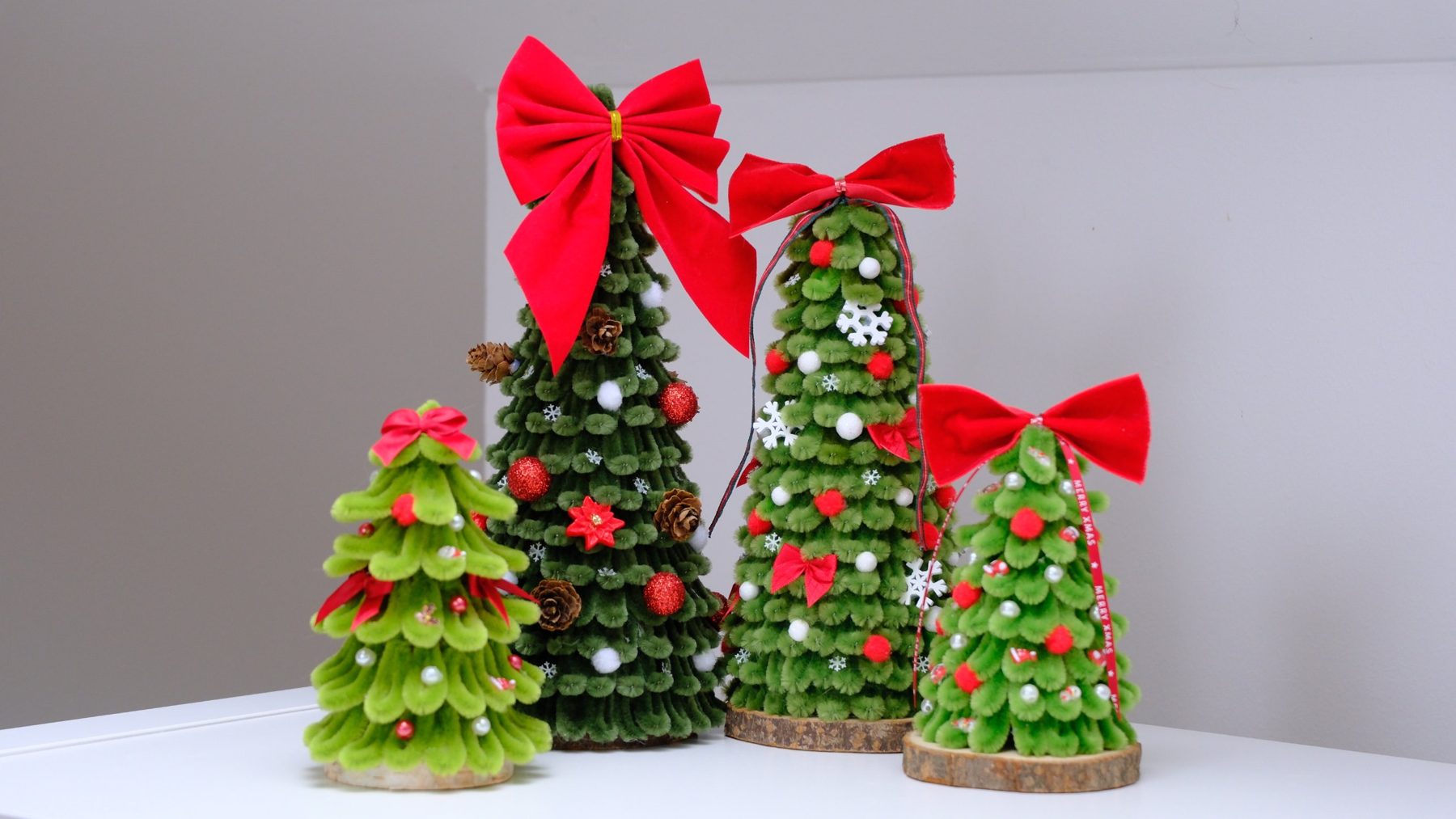 Vier handgemachte Chenille-Weihnachtsbäume mit roten Samtschleifen